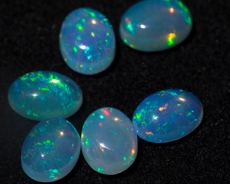 Five polished Ethiopian Welo opal cabochons on black velvet — vivid green/blue/orange pinfire play-of-color across each dome.
