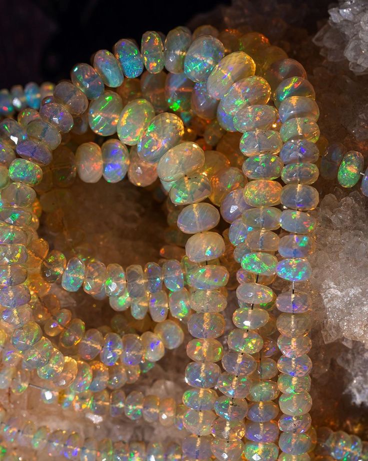 Multiple strands of faceted Welo opal beads coiled on a quartz crystal cluster — vivid green, blue, orange, and violet fire across translucent beads.
